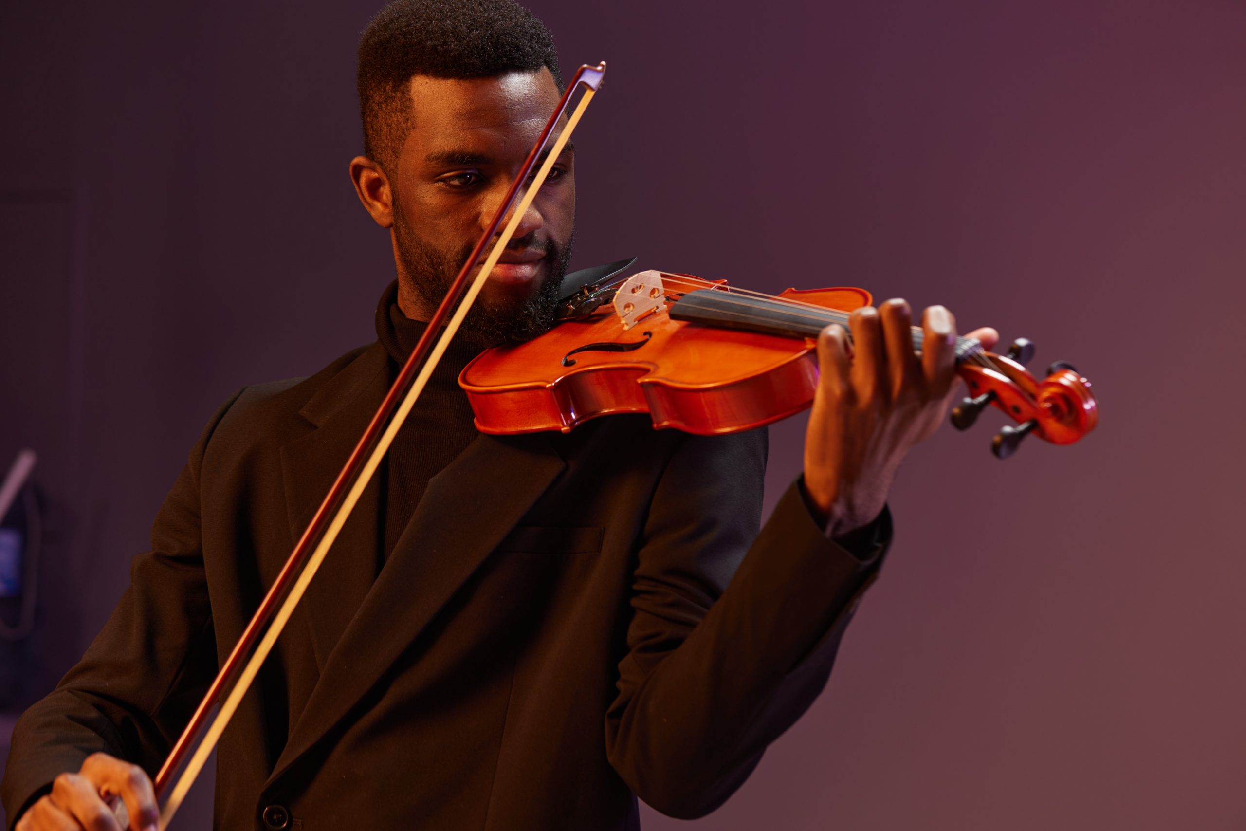 Elegant musician playing violin in black suit on purple stage with dramatic lighting ambiance